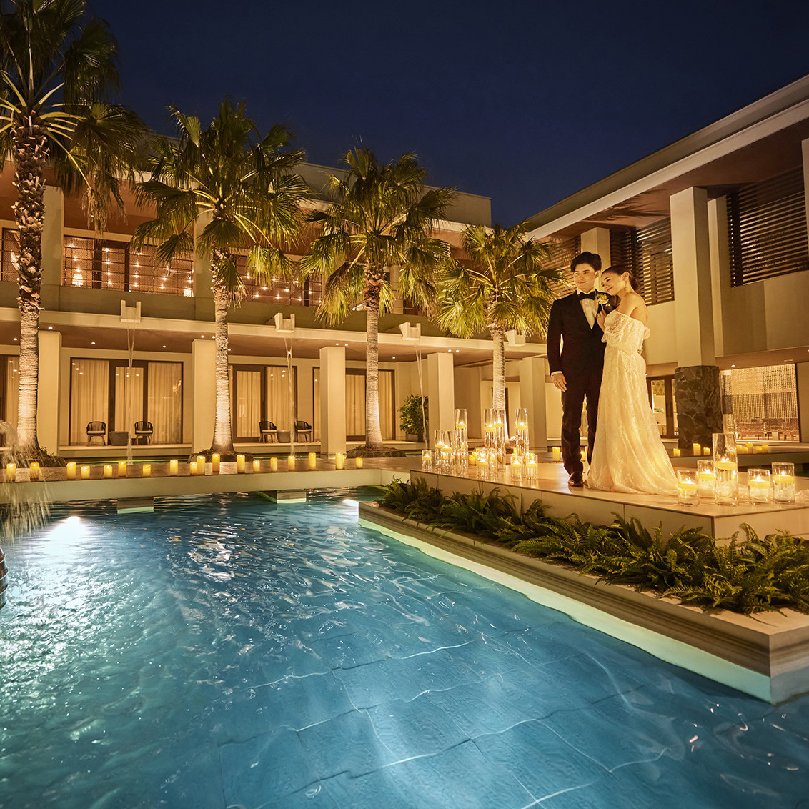 「ライトアップされたプールサイドで寄り添う新郎新婦と、キャンドルが灯るリゾート風のナイトウェディングシーン」