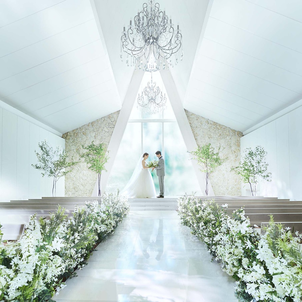 ガラス張りのチャペルで、祭壇に立つ新郎新婦が向かい合うウェディングシーン
